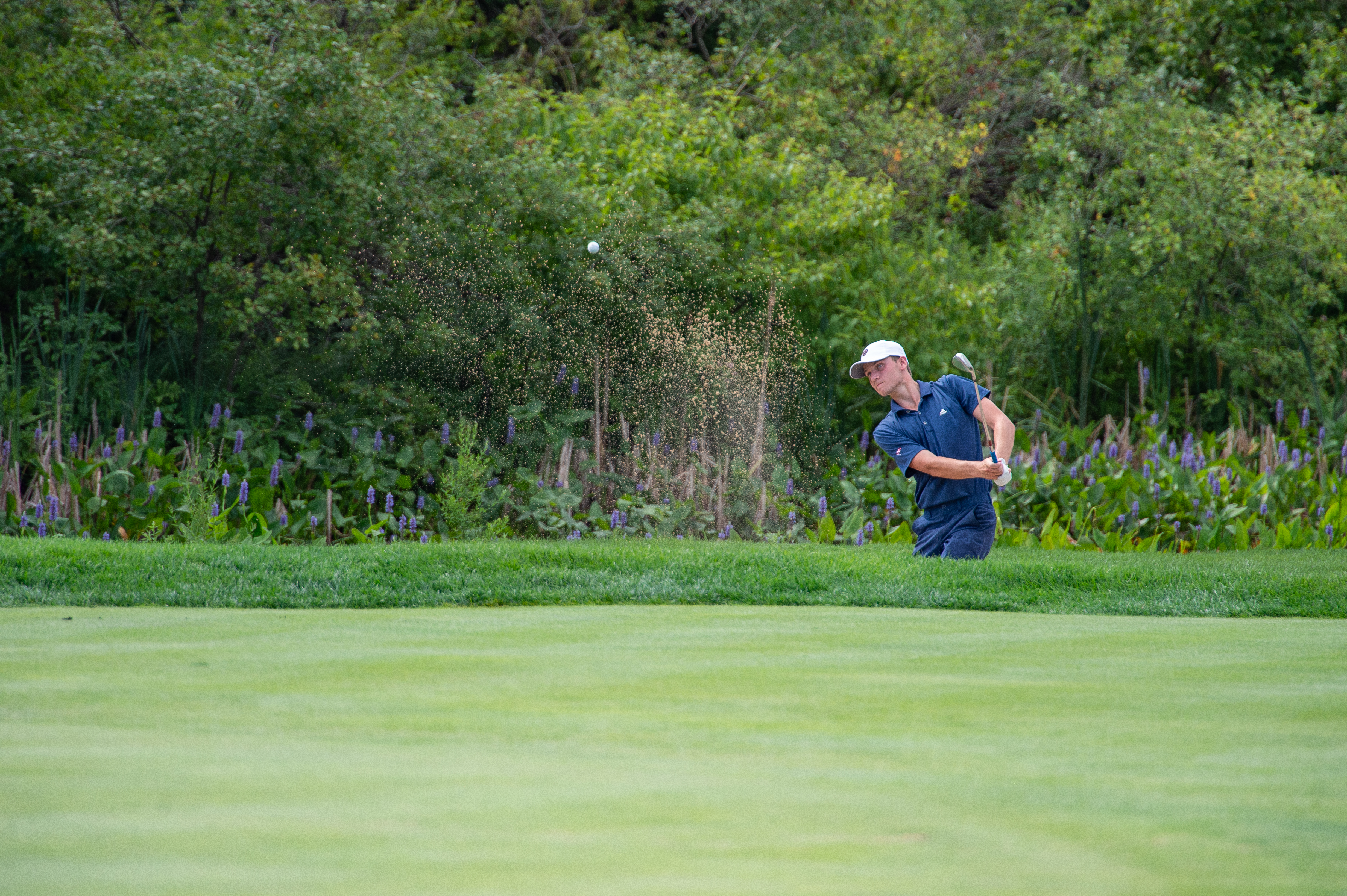 Young male golfer taking a shot out of an unseen bunker.